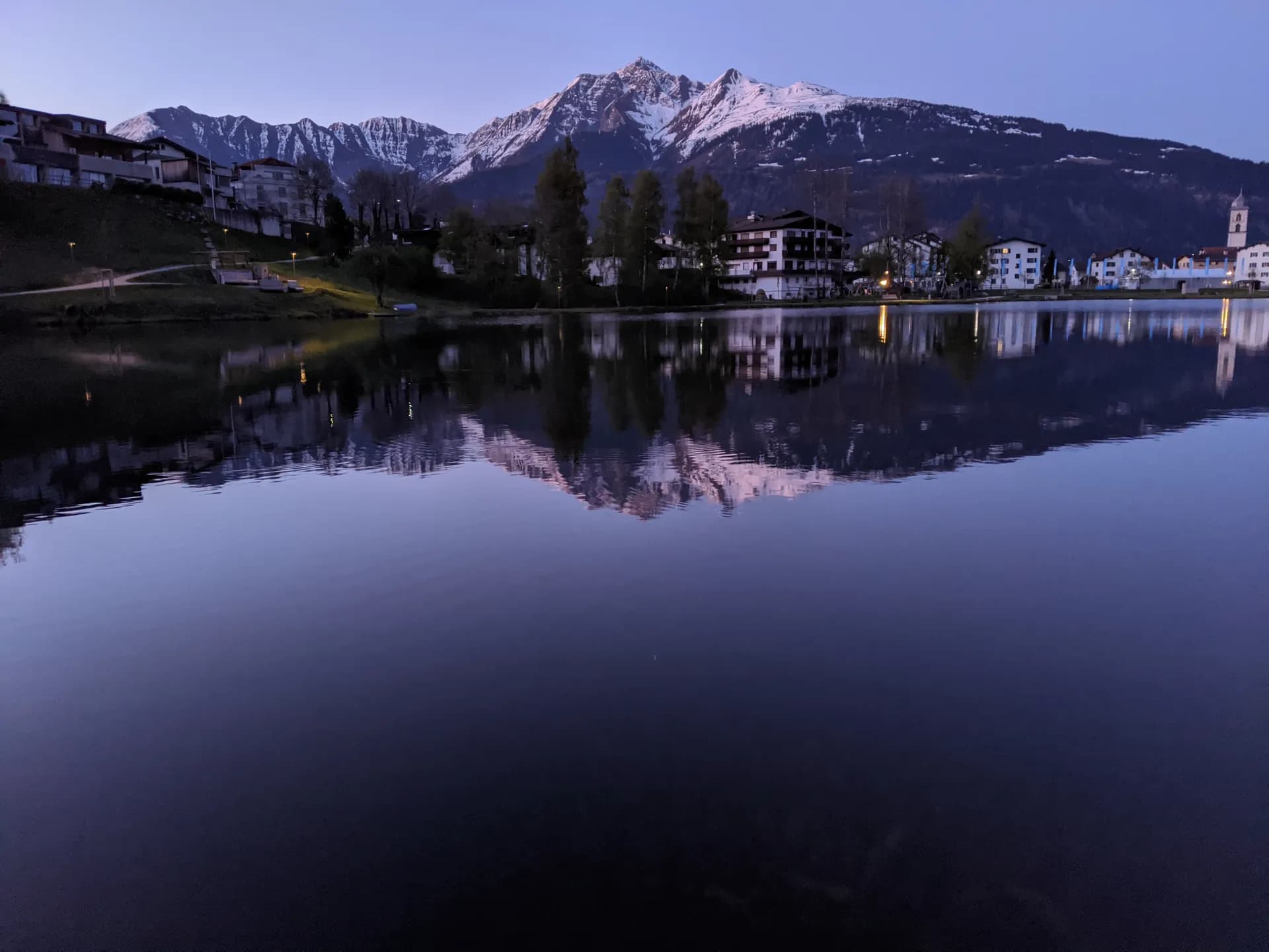 Der Laaxersee im Morgenlicht, dahinter die verschneiten Berge und das Dorf Laax